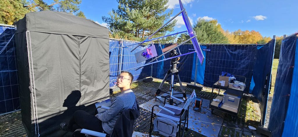 Cheng Li is shown with the outdoor experimental setup. The sunlight concentration module, including the Fresnel lens and the solar concentrator, is mounted on a solar-tracking motor to ensure stable power delivery. The entanglement generation and detection setup, including the nonlinear crystal and the single-photon detectors, are shielded in an optical enclosure placed inside a blackout tent. 