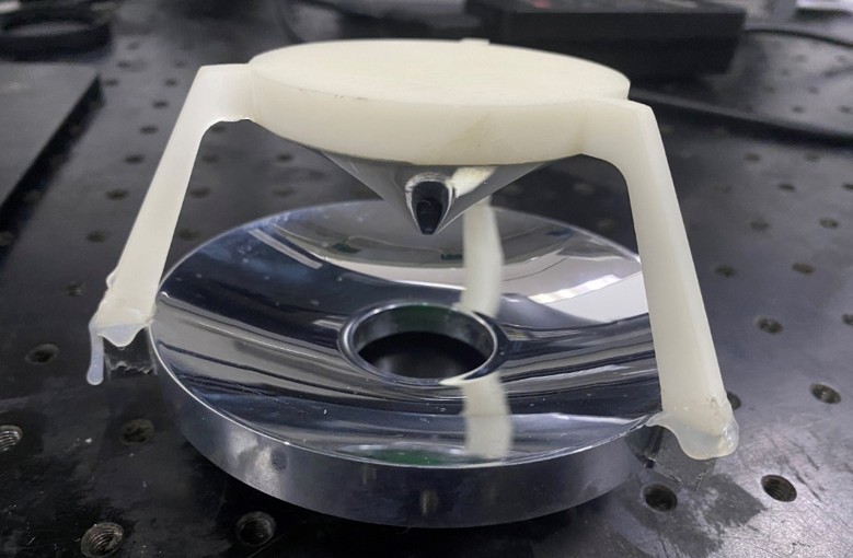A device with a white circular plastic piece above a shiny, circular, mirrored base with a hole in the center.