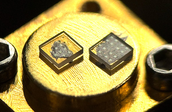 Two small, square hybrid photonic microchips mounted side by side on a circular metallic gold testing stage secured with hex screws.