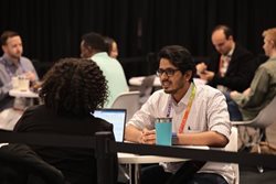 A man and a woman talking at a table with a computer and a mug between them.